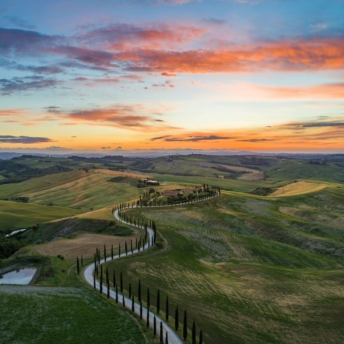 road between green grass field near mountains under blue and brown sky at golden hour